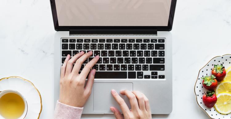 person using laptop with teacup and plate of fruits