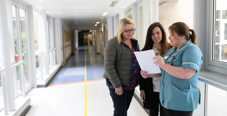 two women with nurse in hospital corridor