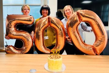 Three women with balloons in the shape of the number 500