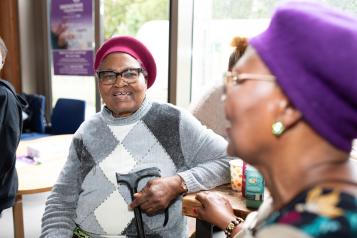 Two older black woman talking and smiling. Both are wearing berets and holding walking sticks.