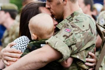 A soldier in army uniform, embracing his partner and child.