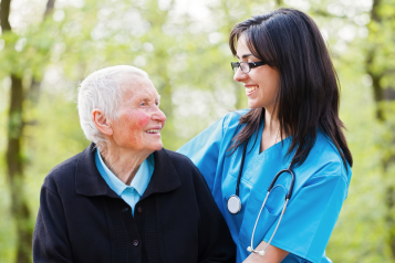 older patient with female nurse standing outside in front of trees