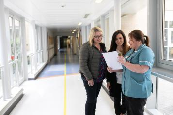 two women with nurse in hospital corridor