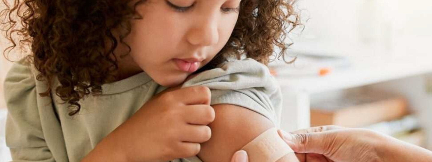 A young child having a small plaster placed on their upper arm.