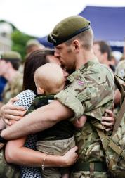 A soldier in army uniform, embracing his partner and child.