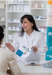 A pharmacist holding a leaflet, talking to a person in a pharmacy.
